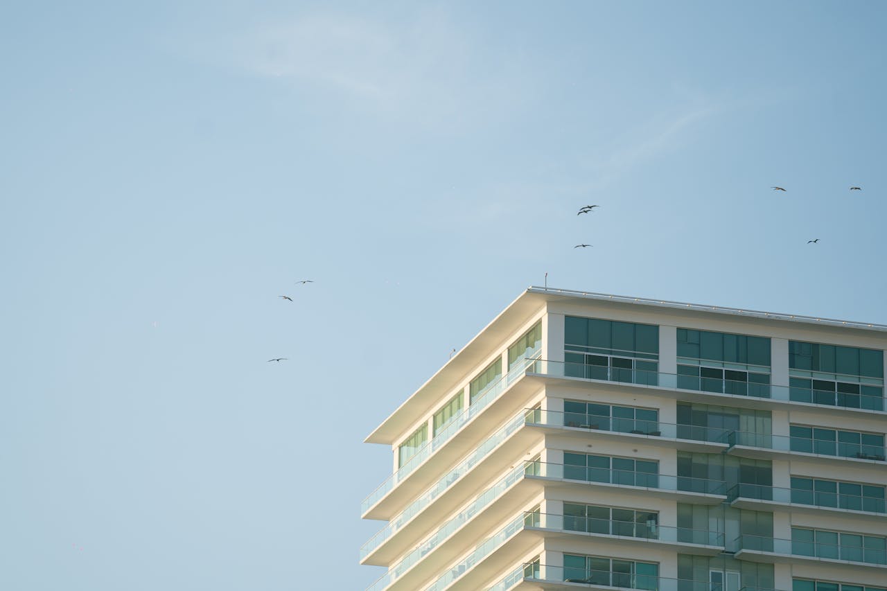 Contemporary glass hotel building against a clear blue sky, with birds flying nearby.